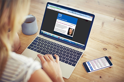 Over the shoulder view of woman using laptop with blank screen. Female blogger is working at home. Smart phone and coffee cup are lying on wooden table.